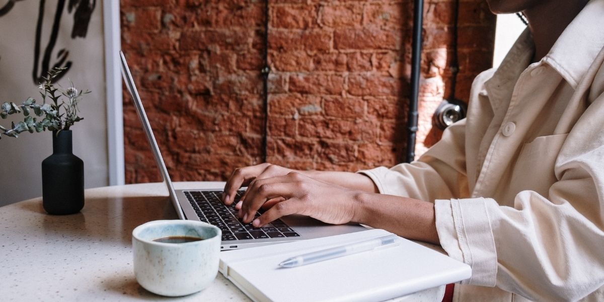Bloggerin sitzt am Tisch mit Laptop, Bullet Journal und Kaffeetasse, WordPress leicht gemacht