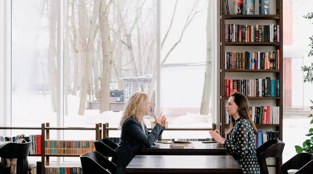 Zwei Frauen sitzen vor einem Bücherregal in einem Café.