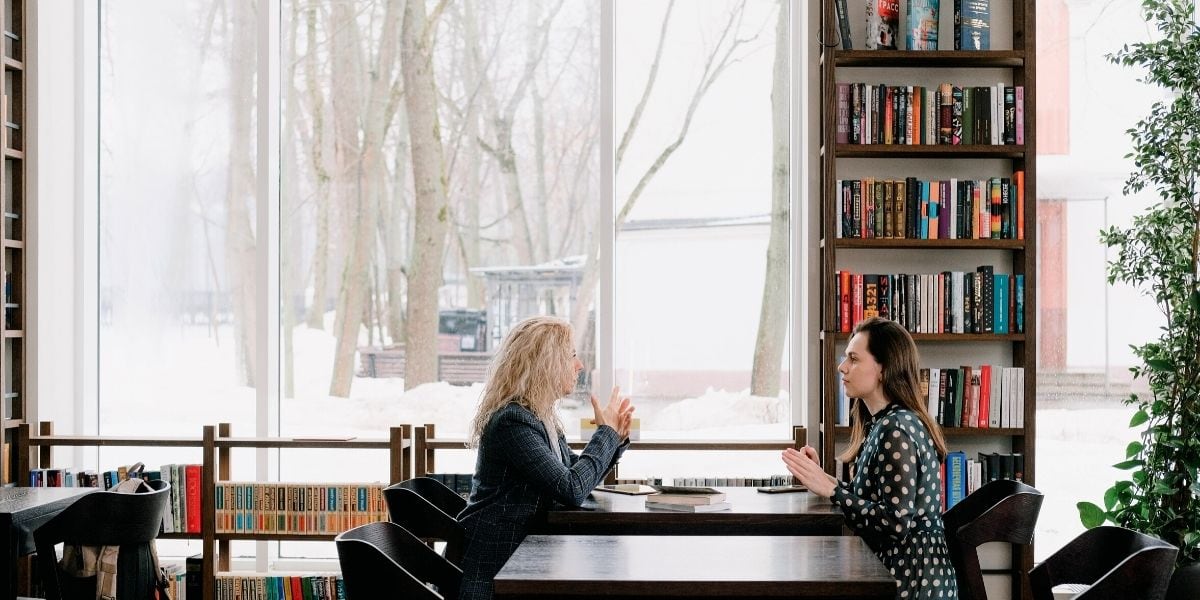 Zwei Frauen sitzen vor einem Bücherregal in einem Café.