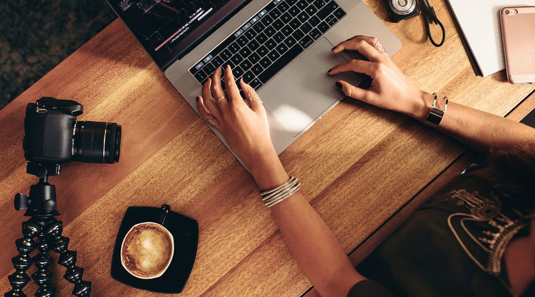 Blog erstellen leicht gemacht, hier Frau am Schreibtisch aus Holz und Laptop, Kaffeetasse, Kamera