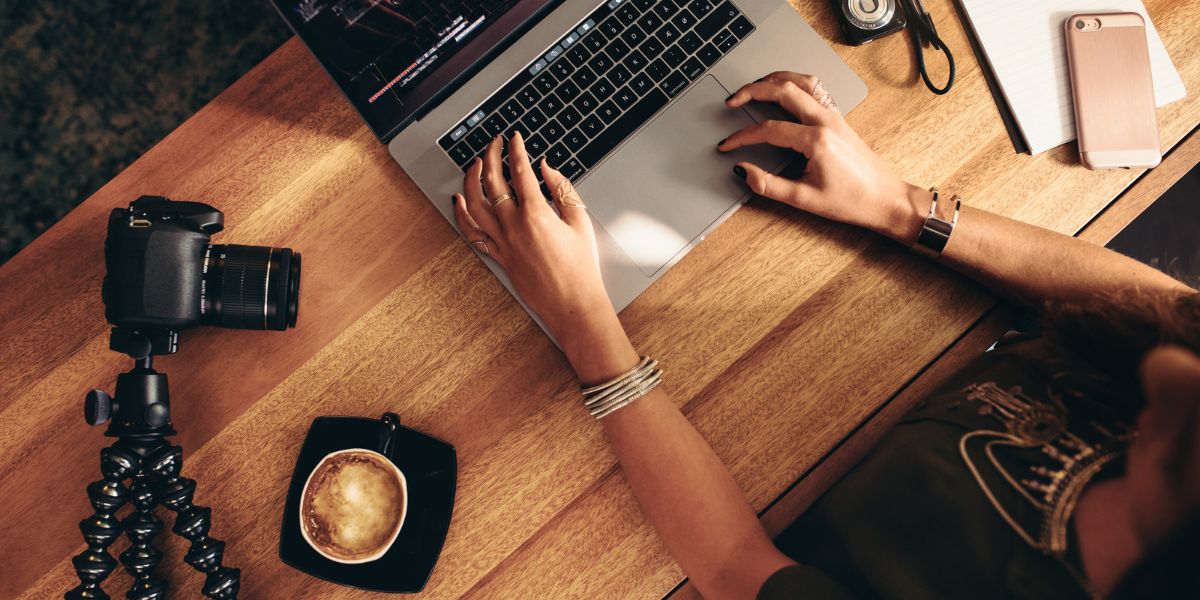 Blog erstellen leicht gemacht, hier Frau am Schreibtisch aus Holz und Laptop, Kaffeetasse, Kamera