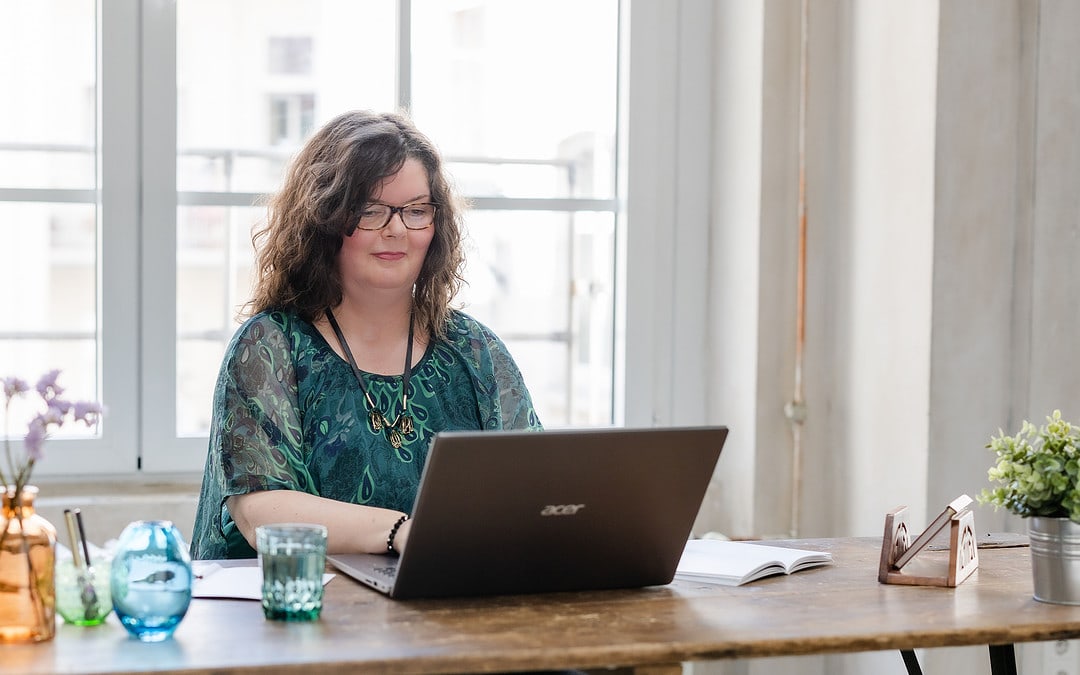 Maria Squarra, hier am Schreibtisch mit Laptop und Wasserglas aus grünem Glas