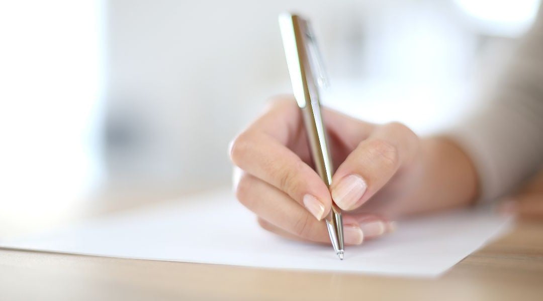 Den richtigen Schreibstil finden, hier gepflegte Frauenhand mit silbernem Kugelschreiber, die ein weißes Blatt Papier beschreibt.