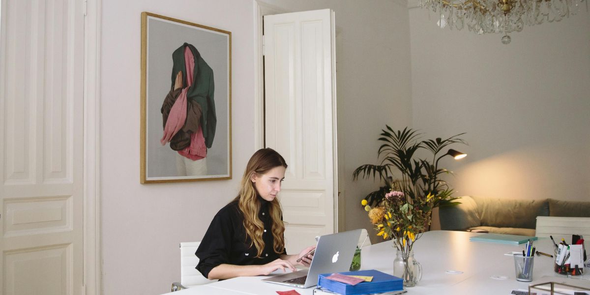 Finde den Namen deiner Blog-Seite, hier junge Frau mit Laptop an großem weißem Schreibtisch, im Hintergrund weiße Altbautüren und ein abstraktes Gemälde