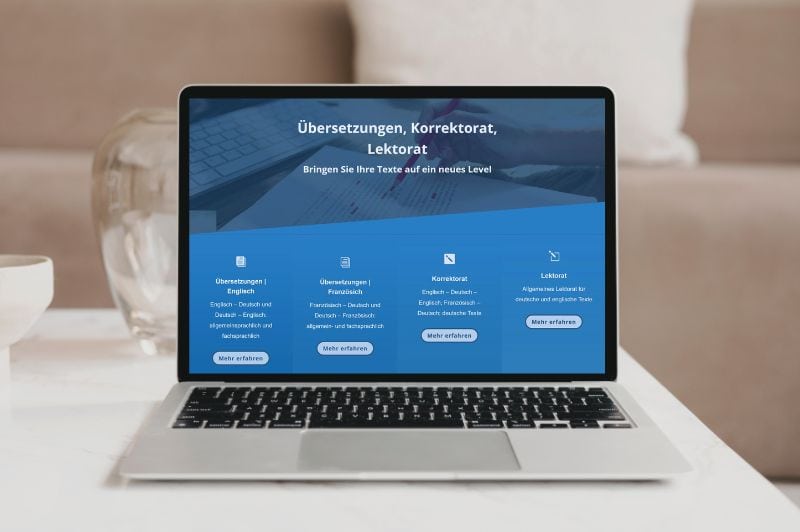 Laptop-Mockup der Website Just-Uebersetzung.de in blauen Farben, Hintergrund weißer Schreibtisch mit Glasvase und beigen Möbeln